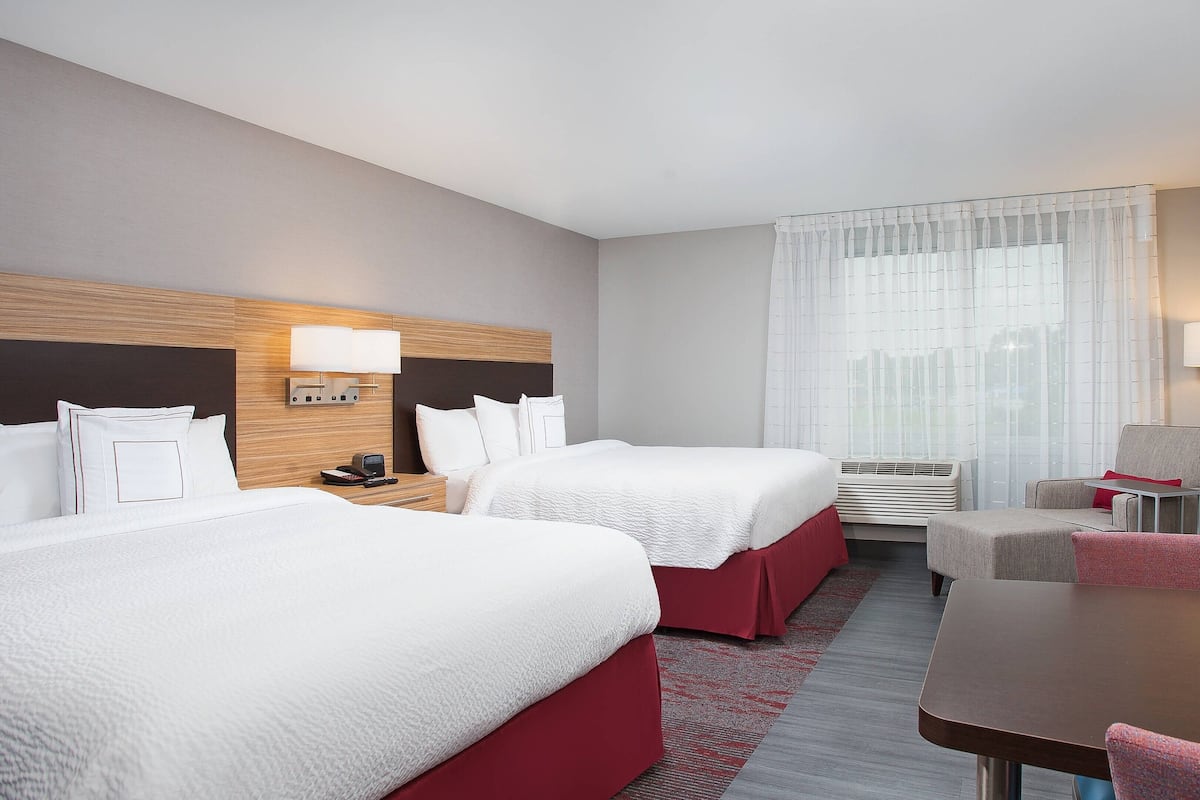 A hotel room with two beds, a desk, a chair, a TV, and a window with curtains.