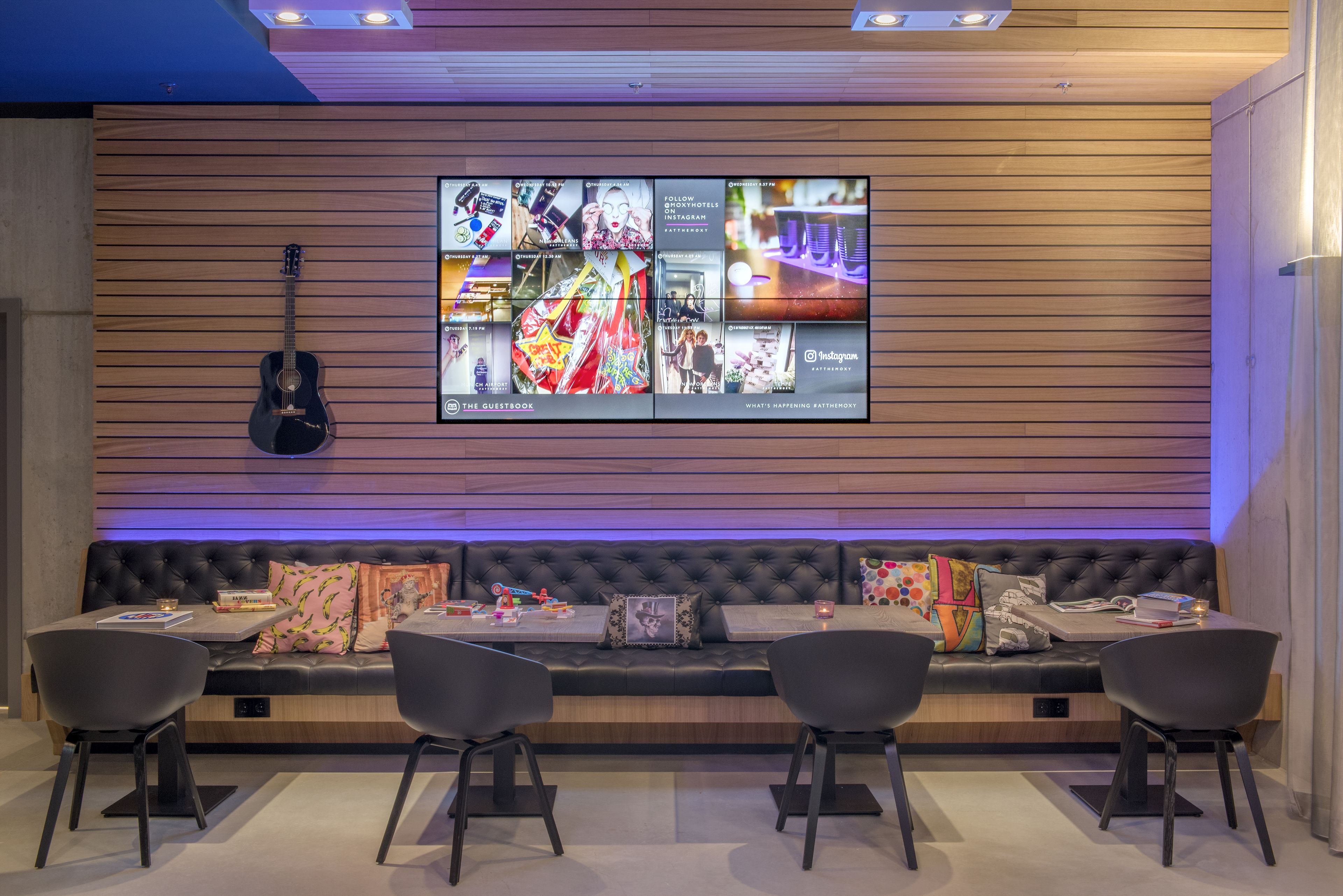 A modern hotel lobby with a large wall-mounted TV displaying various travel destinations.