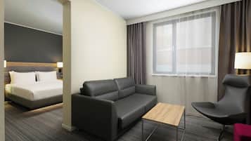 Une chambre d’hôtel avec un lit, un canapé, une chaise, une petite table et une fenêtre avec des rideaux.