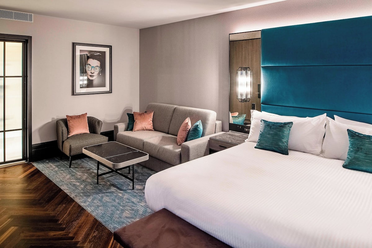 A hotel room with a large bed, two sofas, a coffee table, and a large mirror.