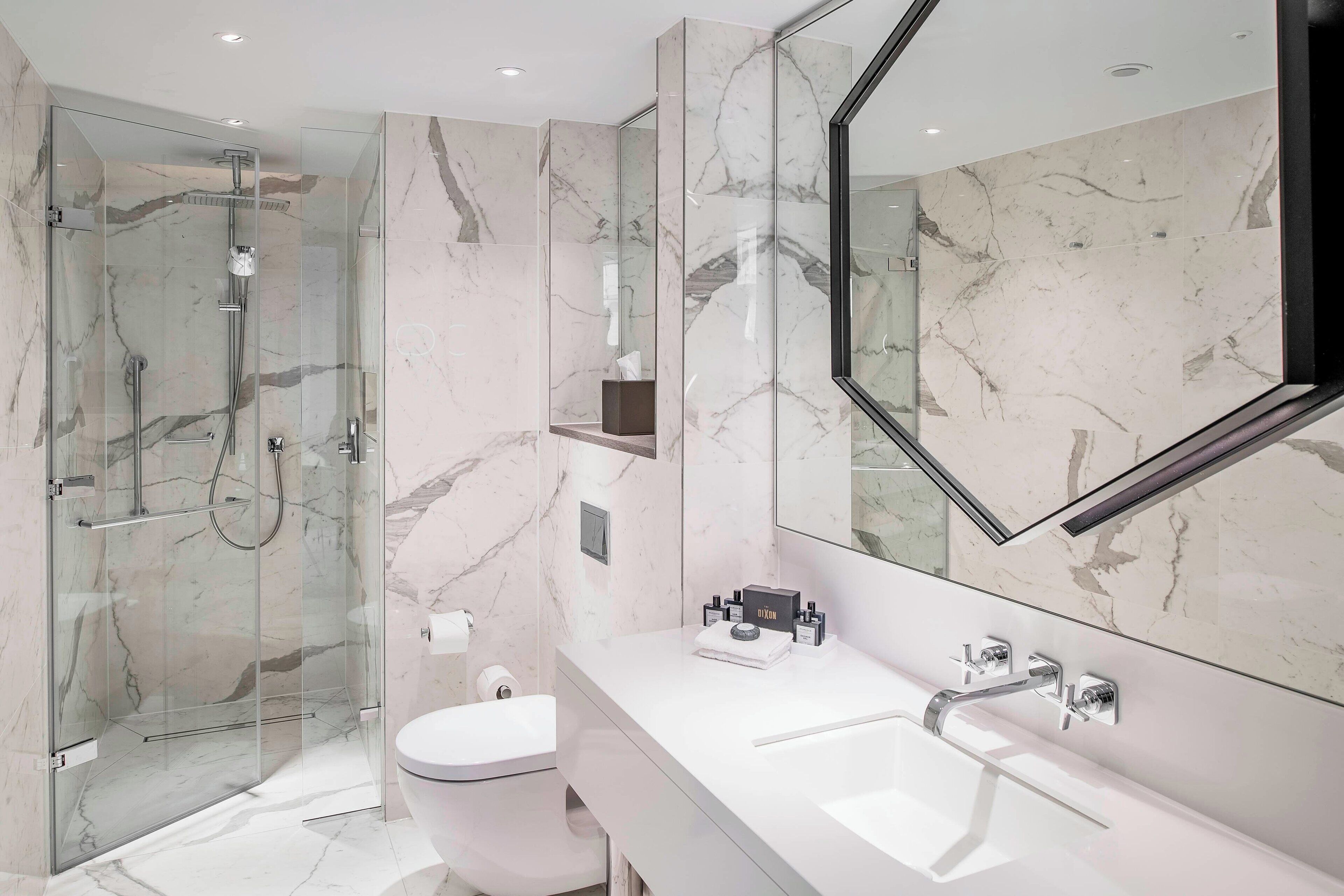 A modern bathroom with a glass-enclosed shower, a white toilet, and a large mirror above a white sink.