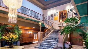 Un vaste hall d’entrée avec un escalier, des œuvres d’art encadrées et des plantes en pot.