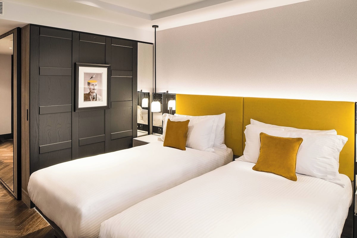 A hotel room with two beds, a large mirror, and a framed picture on the wall.