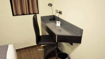 A small room with a desk, chair, and a trash bin.