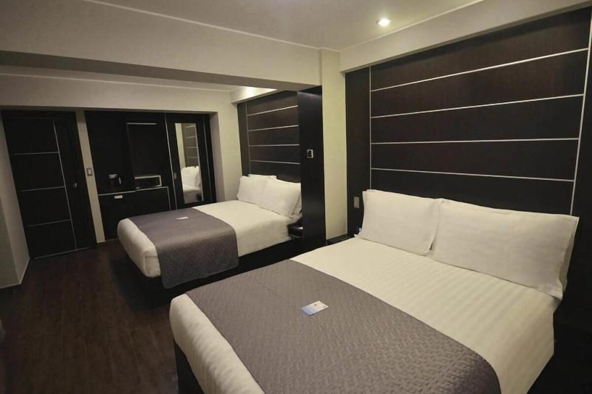 Habitación de hotel con dos camas, cabeceros de madera oscura y un pequeño escritorio.