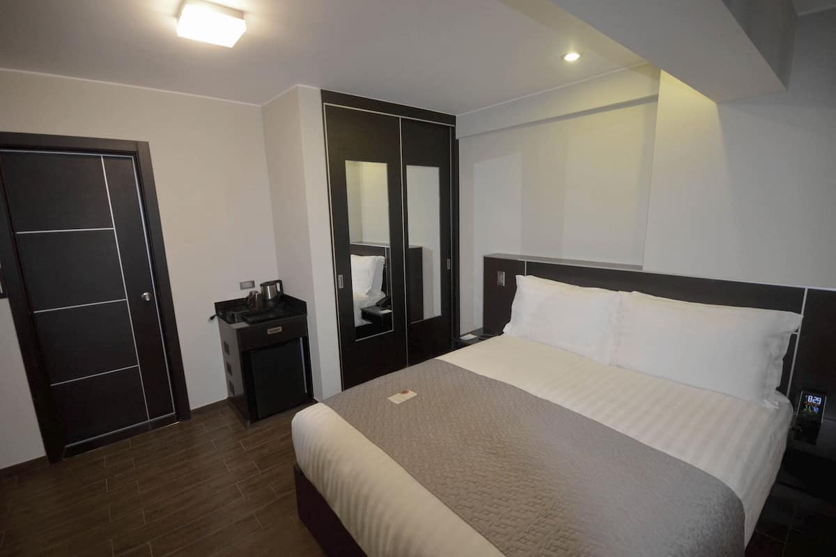Ein modernes Hotelzimmer mit einem großen Bett, einem Schrank, einem Nachttisch und einem Spiegel.