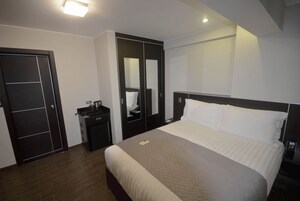 A modern hotel room with a large bed, a wardrobe, a bedside table, and a mirror.