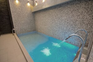 Una piscina con agua cristalina azul, una escalera metálica y suelo de baldosas.