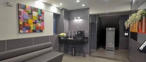 A modern hotel lobby with a gray bench, a colorful abstract painting, a small bar area, and a refrigerator.