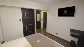 A hotel room with a bed, a TV mounted on the wall, and a door leading to another room.