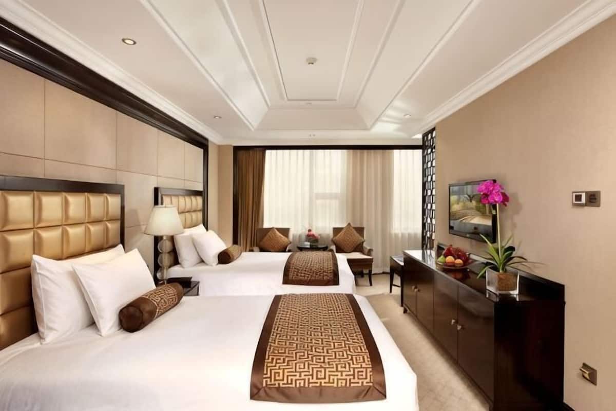 A hotel room with two beds, a desk, a TV, and a large window.