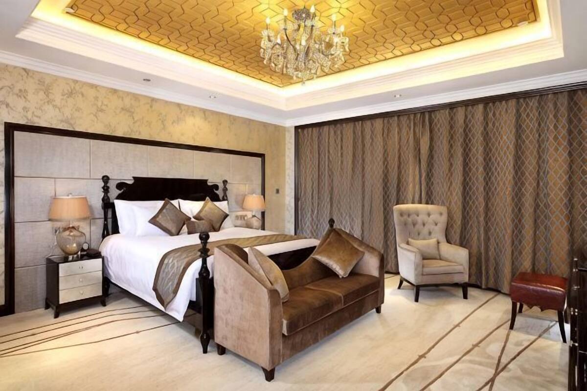 A bedroom with a large bed, a chair, a nightstand, and a chandelier.