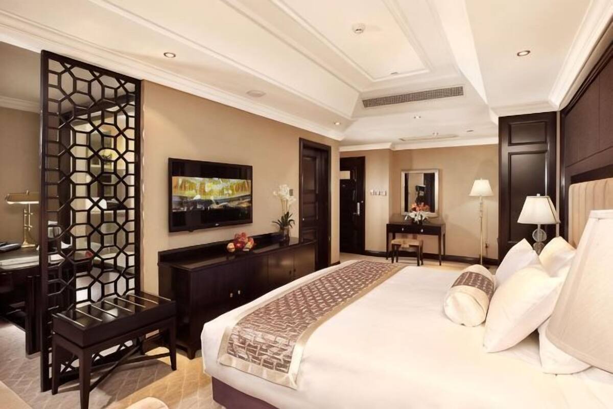 A hotel room with a large bed, a TV, a desk, and a decorative screen.