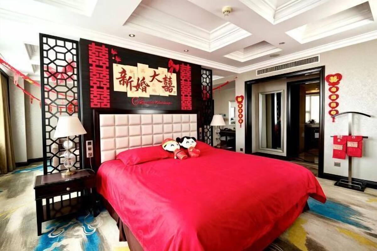 A hotel room with a large bed, decorative wall panels, and a red bedspread.