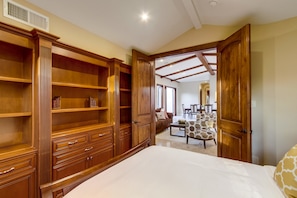 Une chambre avec un grand lit, une armoire en bois et un coin repas avec des chaises à motifs.