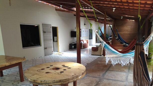 A cozy living area with a hammock, a round wooden table, and a TV on the wall. - Hostel Lençóis Park (Barreirinhas)