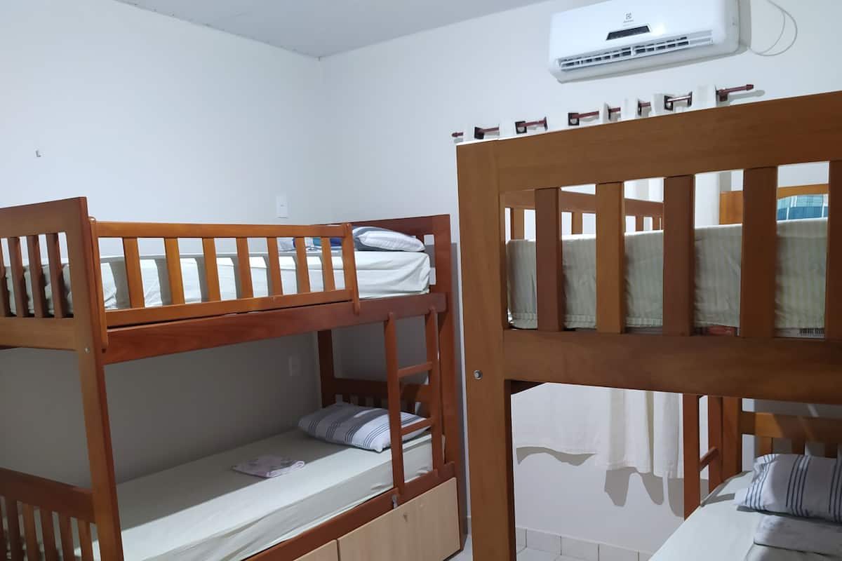 A room with two bunk beds, a white air conditioning unit on the wall, and a window with a view of parked cars.