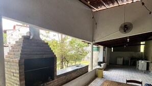 An outdoor patio with a brick fireplace, a wooden table, and patterned floor tiles. - Hostel Lençóis Park (Barreirinhas)
