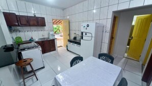 A compact kitchen with white tiles, a refrigerator, a stove, and a dining area with a table and chairs. - Hostel Lençóis Park (Barreirinhas)
