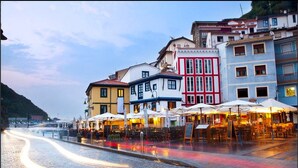 A cobblestone street lined with colorful buildings, outdoor seating areas, and a view of a body of water. - LA Nana DEL MAR Flat on the old Port of Cudillero (Cudillero)