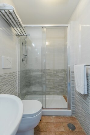 A bathroom with a glass-enclosed shower, a white toilet, and a towel rack. - Walker Rooms (Rome)