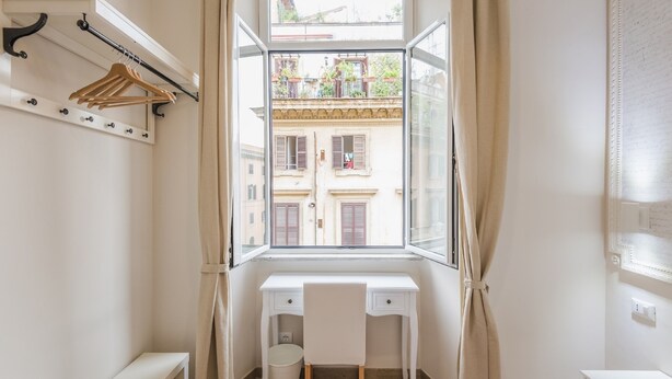 A small, bright room with a white desk and a window overlooking a building. - Walker Rooms (Rome)