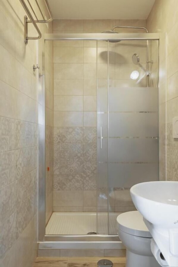 Ducha con puerta de vidrio, inodoro y azulejos con diseño.