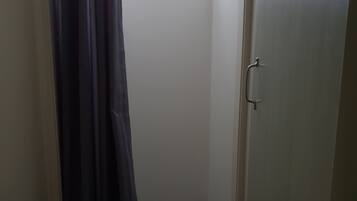 A small, narrow bathroom with a shower area, a door with a handle, and a window allowing natural light.