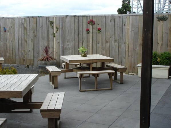 An outdoor patio with a wooden table and benches, surrounded by a wooden fence with decorative elements. - Horse and Jockey Inn (Matamata)