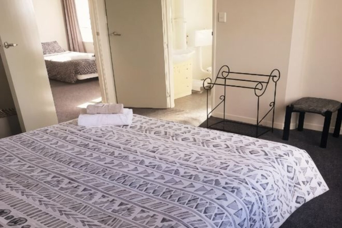 A hotel room with a bed, a small bench, and a door leading to another room.