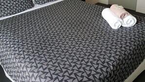 A neatly made bed with a patterned bedspread, pillows, and a rolled towel on the bed. - Horse and Jockey Inn (Matamata)