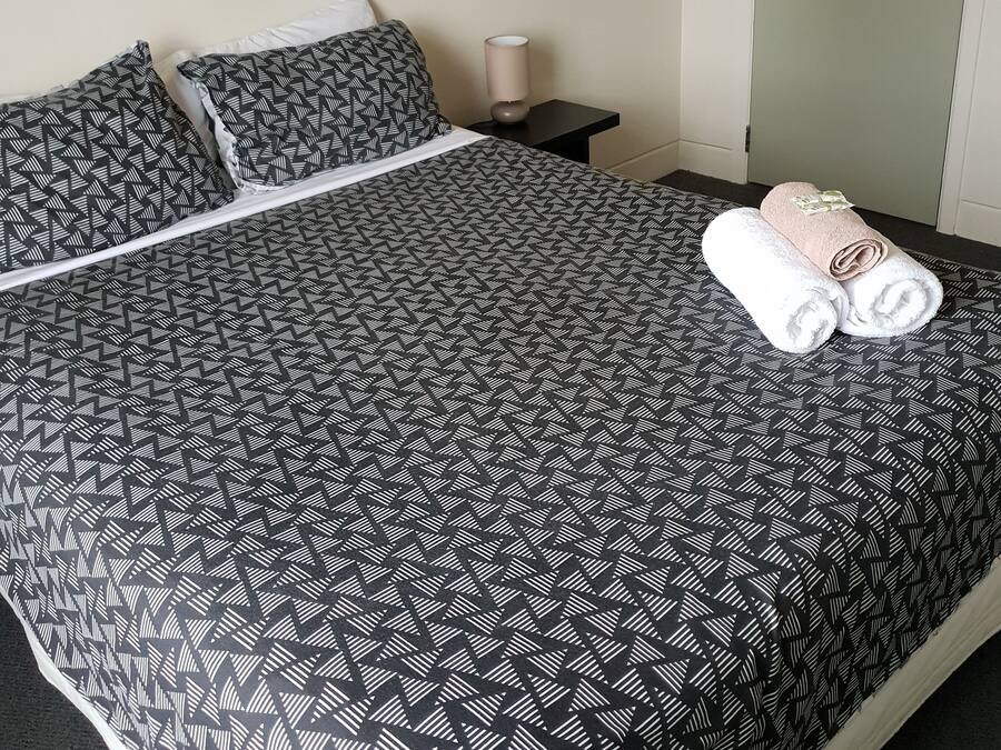 A neatly made bed with a patterned bedspread, pillows, and a rolled towel on the bed.