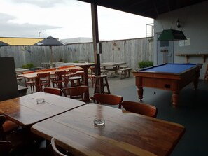 An outdoor seating area with wooden tables and chairs, a pool table, and a wooden fence. - Horse and Jockey Inn (Matamata)