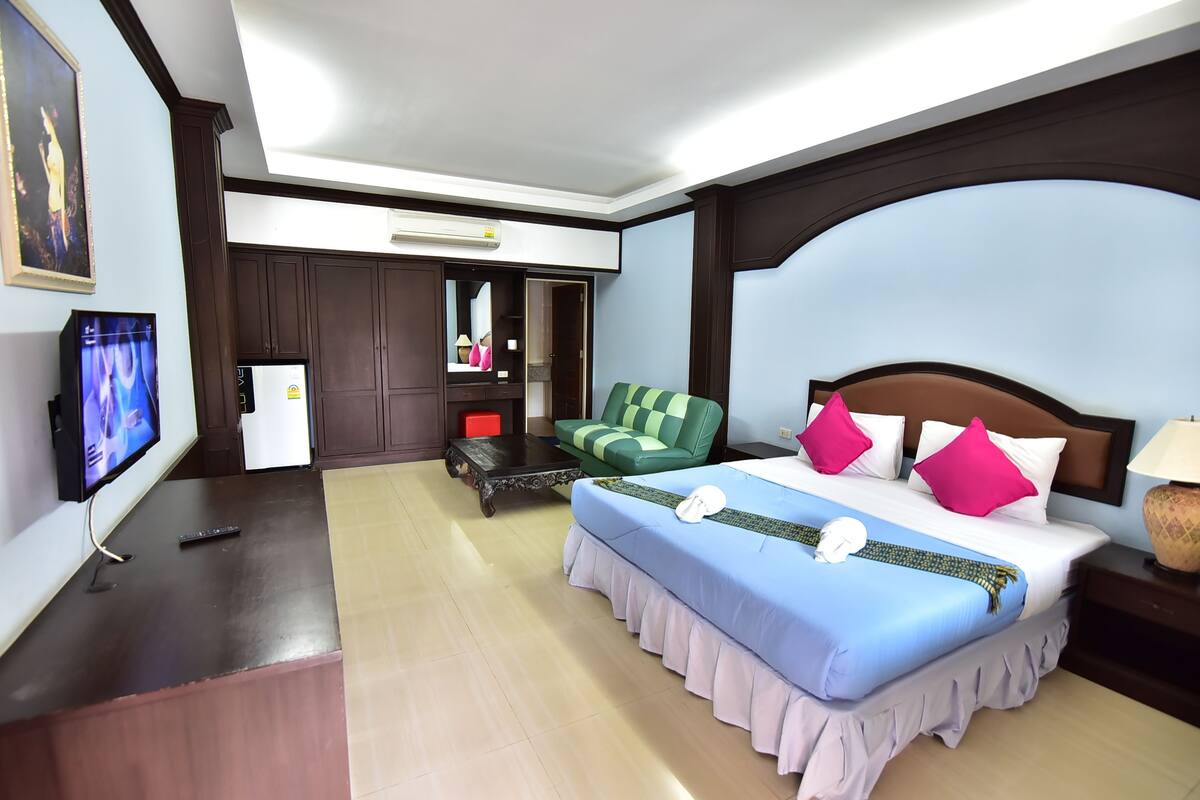 A hotel room with a large bed, a TV, a desk, and a wardrobe.