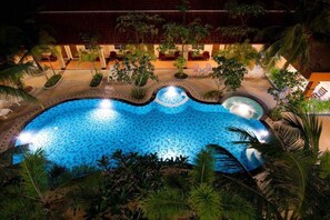 A swimming pool with a tiled edge, surrounded by palm trees and a covered seating area with chairs. - Ampan Resort (Pattaya)