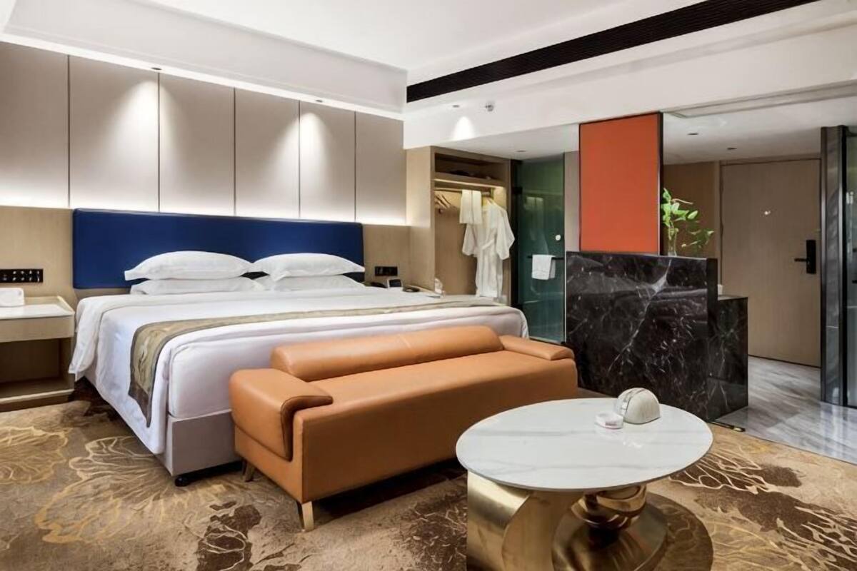 A modern hotel room with a large bed, a sofa, a round table, and a bathroom visible through an open door.
