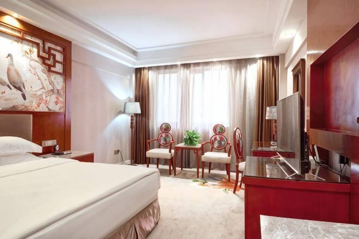 A hotel room with a bed, a desk with a chair, a TV, and a painting on the wall.