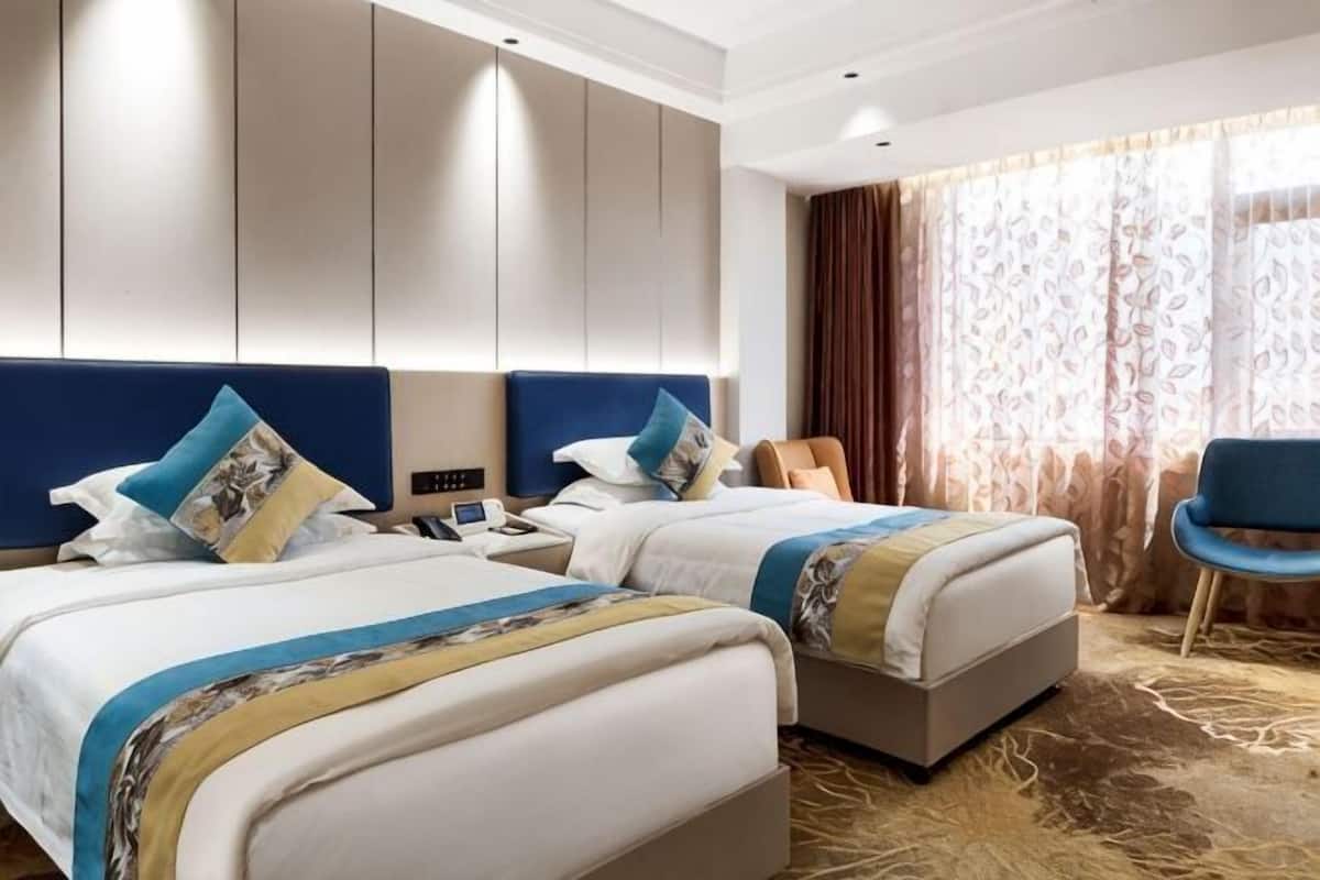 A hotel room with two beds, a desk, a chair, and a large window with curtains.