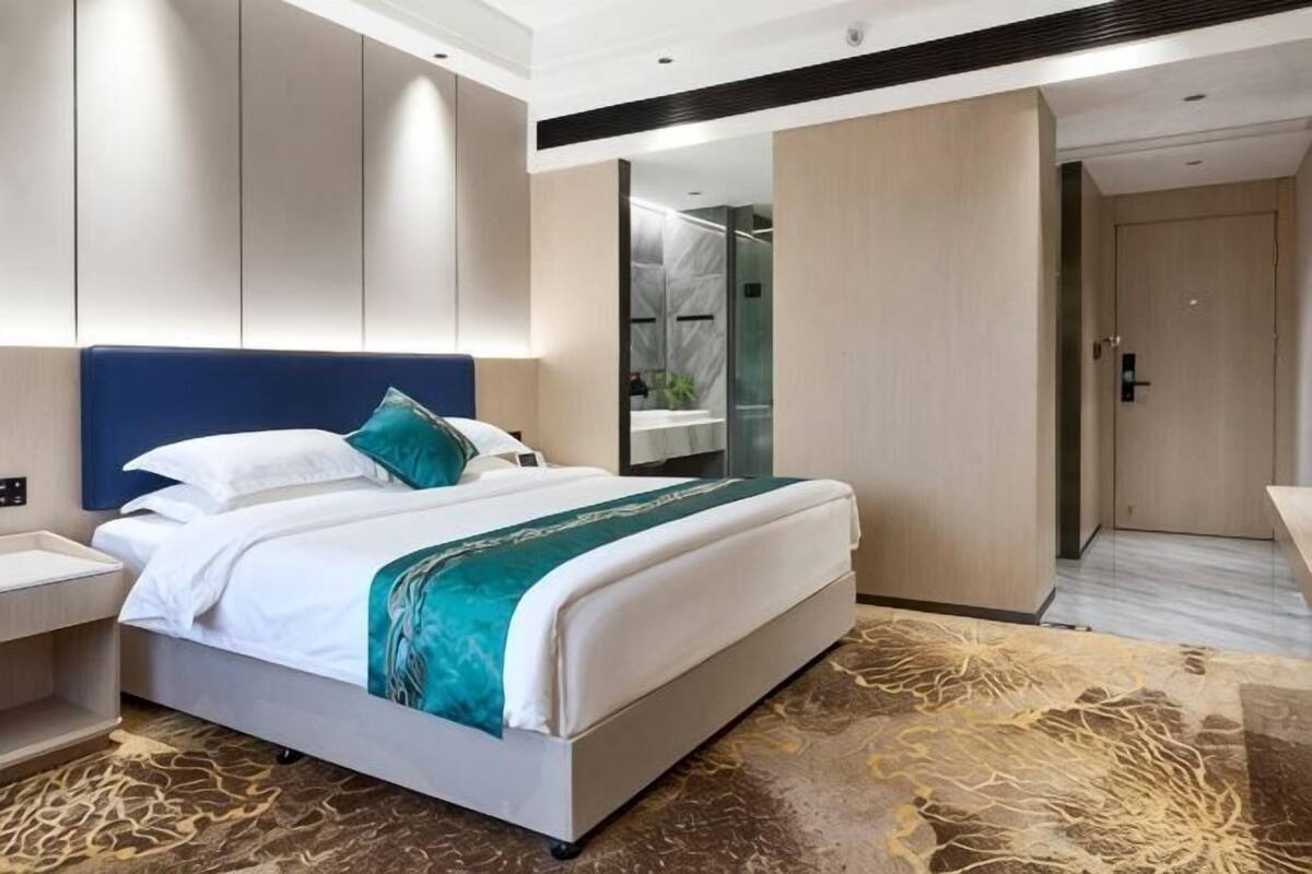 A modern hotel room with a large bed, a nightstand, a bathroom mirror, and a door leading to another room.