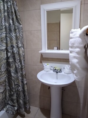 Un baño con un lavamanos blanco, un espejo encima y una cortina de ducha estampada.