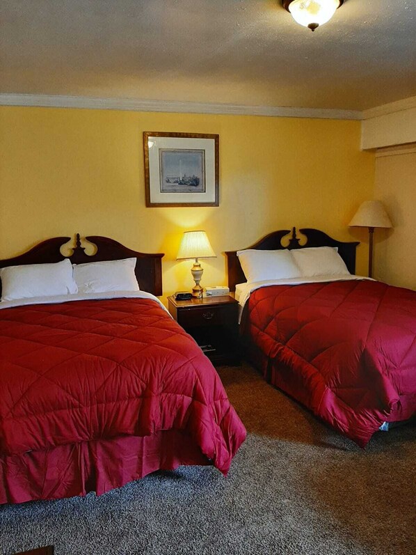 Habitación de hotel con dos camas, cada una con colcha acolchada roja y almohadas blancas. Hay un cuadro en la pared sobre las camas y una lámpara en la mesita de noche entre ellas.