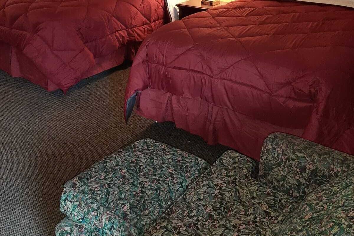 Habitación de hotel con dos camas, una mesita de noche con lámpara, un cuadro enmarcado en la pared y un banco estampado con motivos florales.