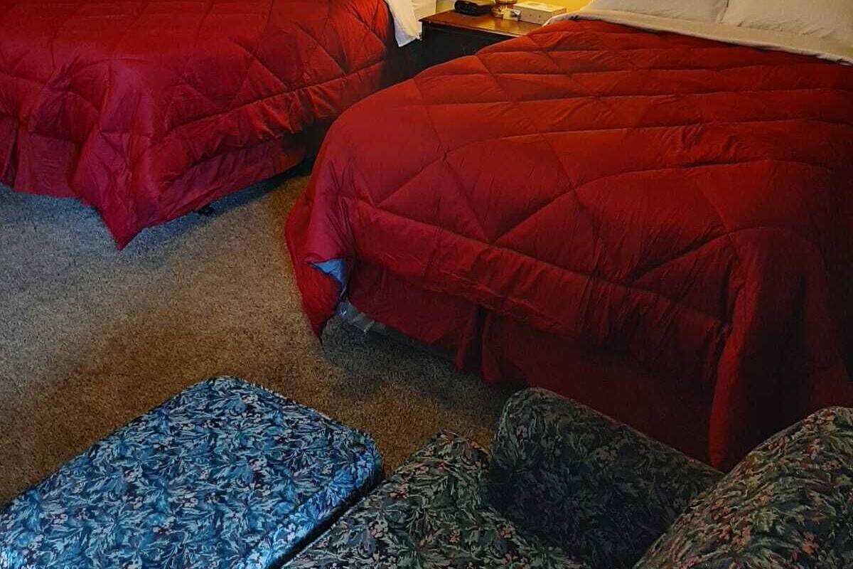 Habitación de hotel con dos camas, una mesita de noche con lámpara, un cuadro enmarcado en la pared y un banco con estampado floral.