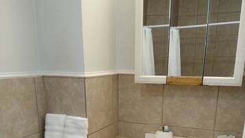 Un baño con inodoro, lavamanos y espejo. Hay toallas apiladas en la pared y una barra de cortina de ducha sobre el espejo.