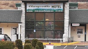 A motel with a large sign reading "Clarysville Motel" and a website address. There is a parking lot in front and a small office building to the right.