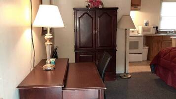 Habitación de hotel compacta con un escritorio de madera, una silla, televisor montado en la pared, armario y zona de kitchenette.