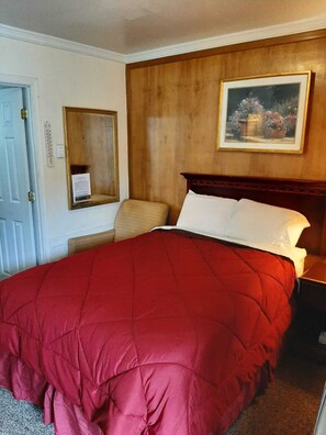 Habitación de hotel con una cama grande, cabecera de madera, un cuadro en la pared, una mesita de noche y una puerta con termostato.
