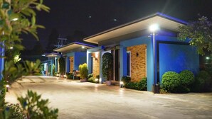 Una fila de habitaciones de hotel modernas con un estilo arquitectónico uniforme, con paredes exteriores de ladrillo y azul, y un área exterior cubierta con plantas en macetas.