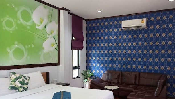 Habitación de hotel con una cama grande, un sofá marrón, un aire acondicionado de pared y una ventana con vistas.
