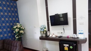 Una zona de recepción con un televisor montado en la pared, un escritorio con hervidor, flores y botellas de agua.
